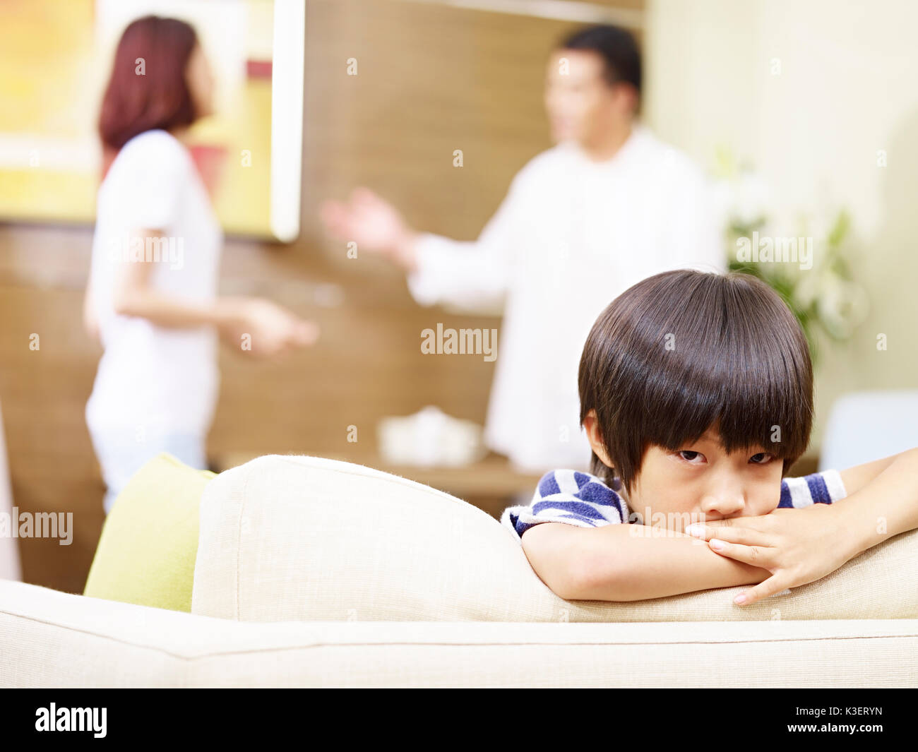 Bambino asiatico sembra triste e infelice mentre i genitori quarreling in background. Foto Stock