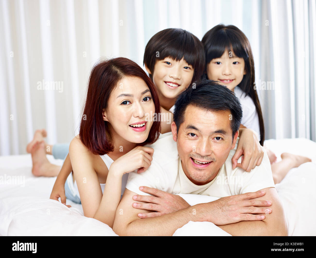Felice famiglia asiatica con due bambini che si divertono nel letto di casa. Foto Stock