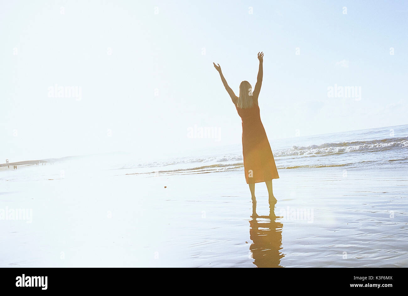 La donna si erge in riva al mare e allunga le braccia in aria Foto Stock