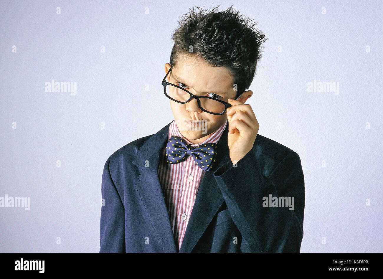 Piccolo Ragazzo con il filtro bow tie tocca con mano la montatura degli occhiali e tira la sua bocca Foto Stock