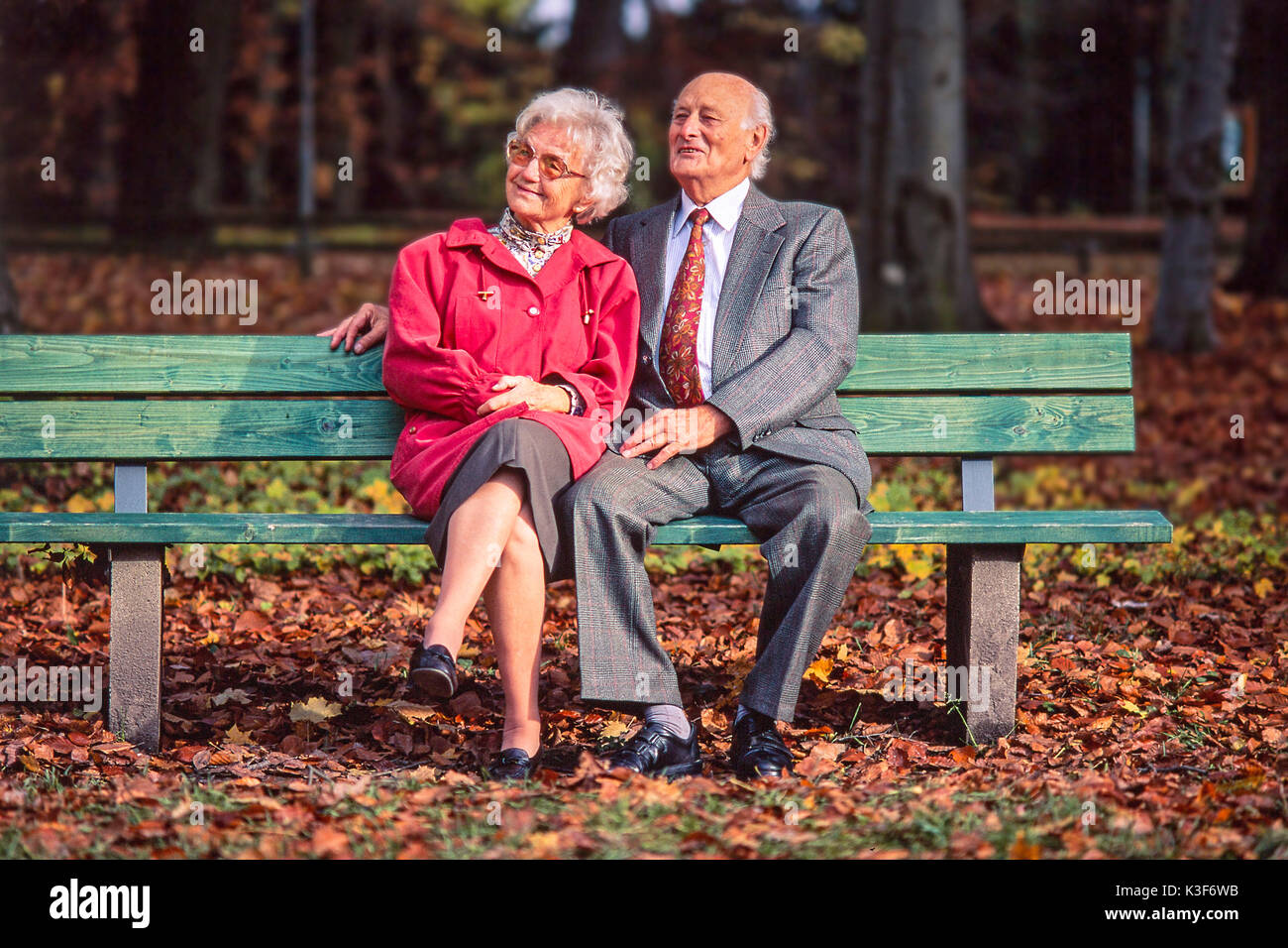 Senior Citizen's giovane siede insieme su una panca in legno in legno Foto Stock