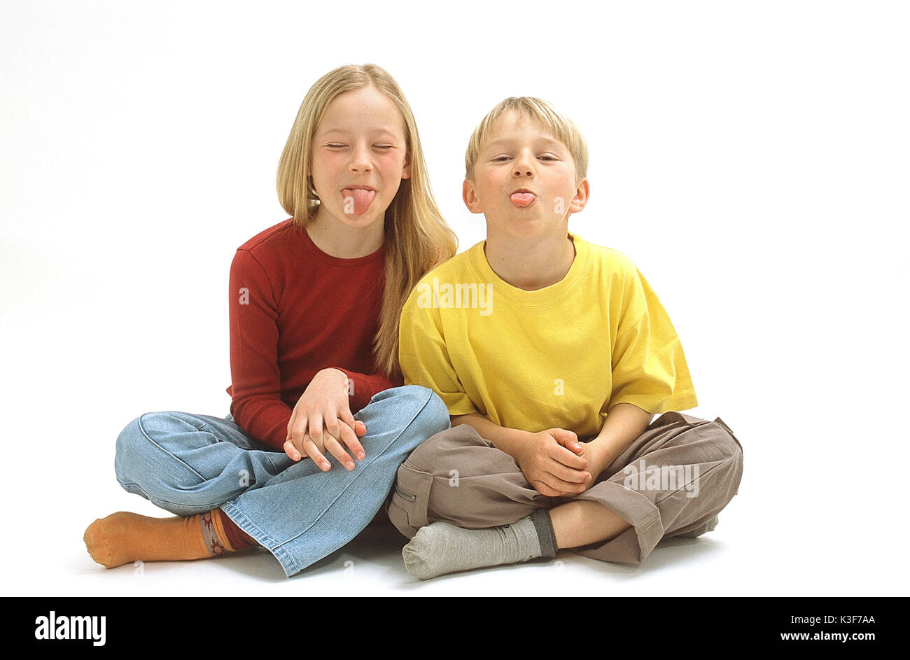 Ragazzo e una ragazza sedersi a gambe incrociate e attaccare la lingua di fuori Foto Stock