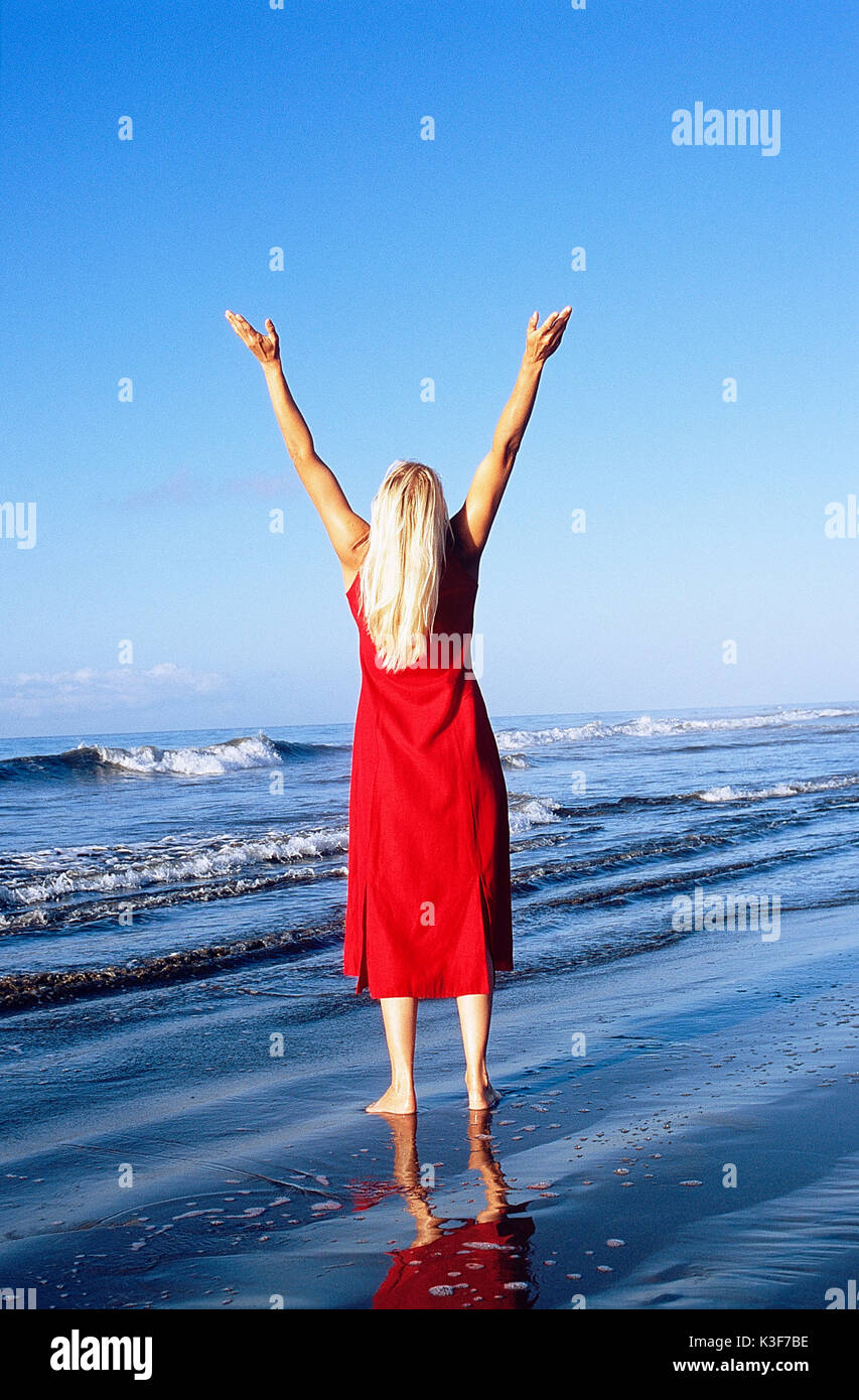 La donna si erge in riva al mare e allunga le braccia in aria Foto Stock