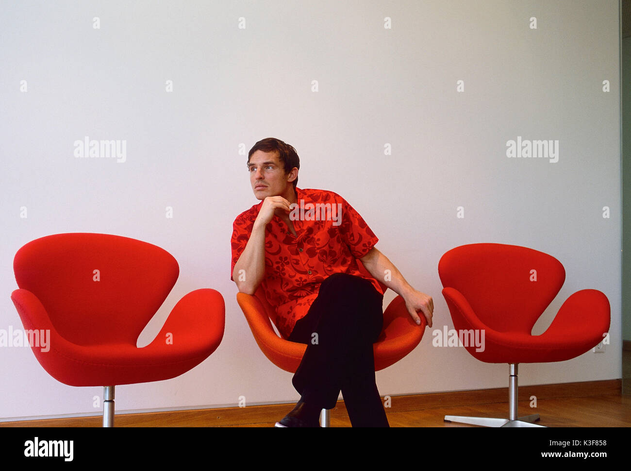 Giovane uomo si siede pensieroso / annoiato in poltrona orangem Foto Stock