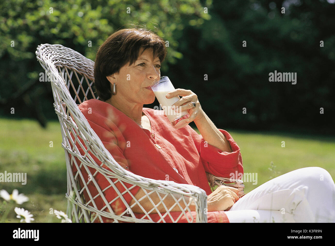 La donna si siede nel giardino e beve un bicchiere di latte Foto Stock
