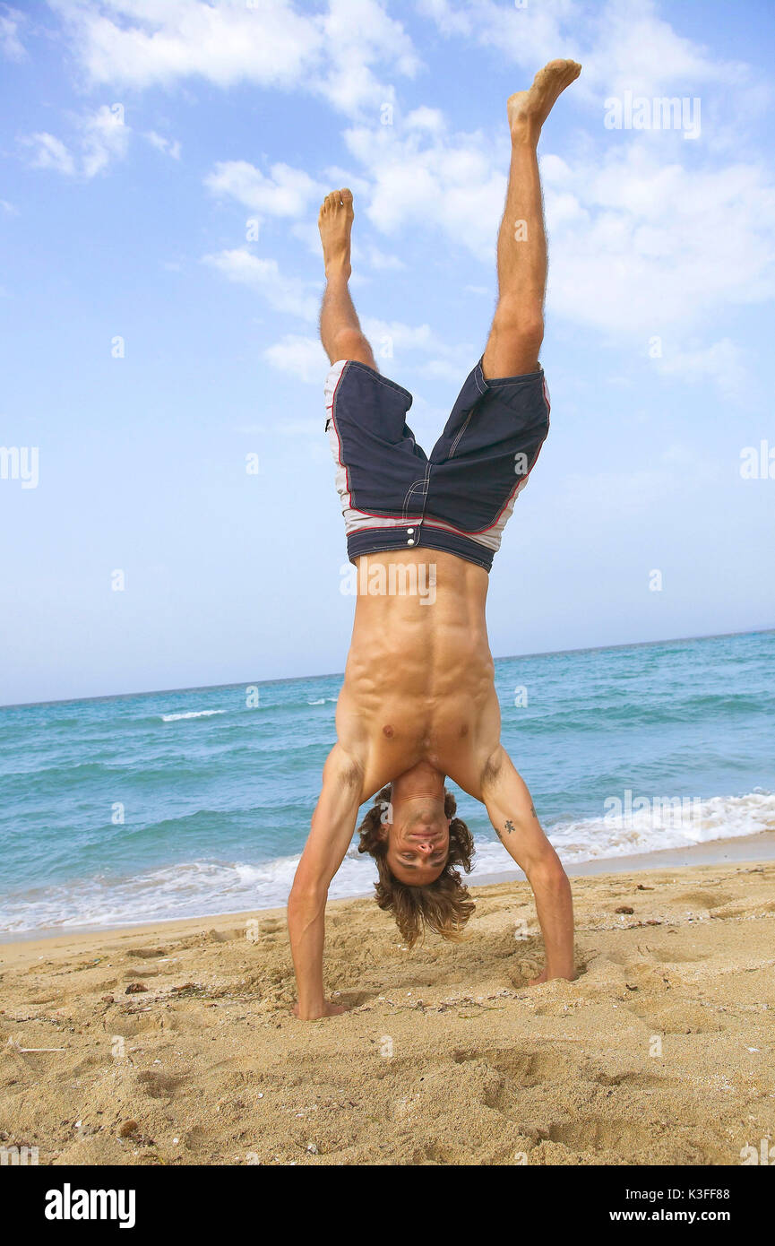 Uomo con tronchi di nuoto in handstand in spiaggia Foto Stock