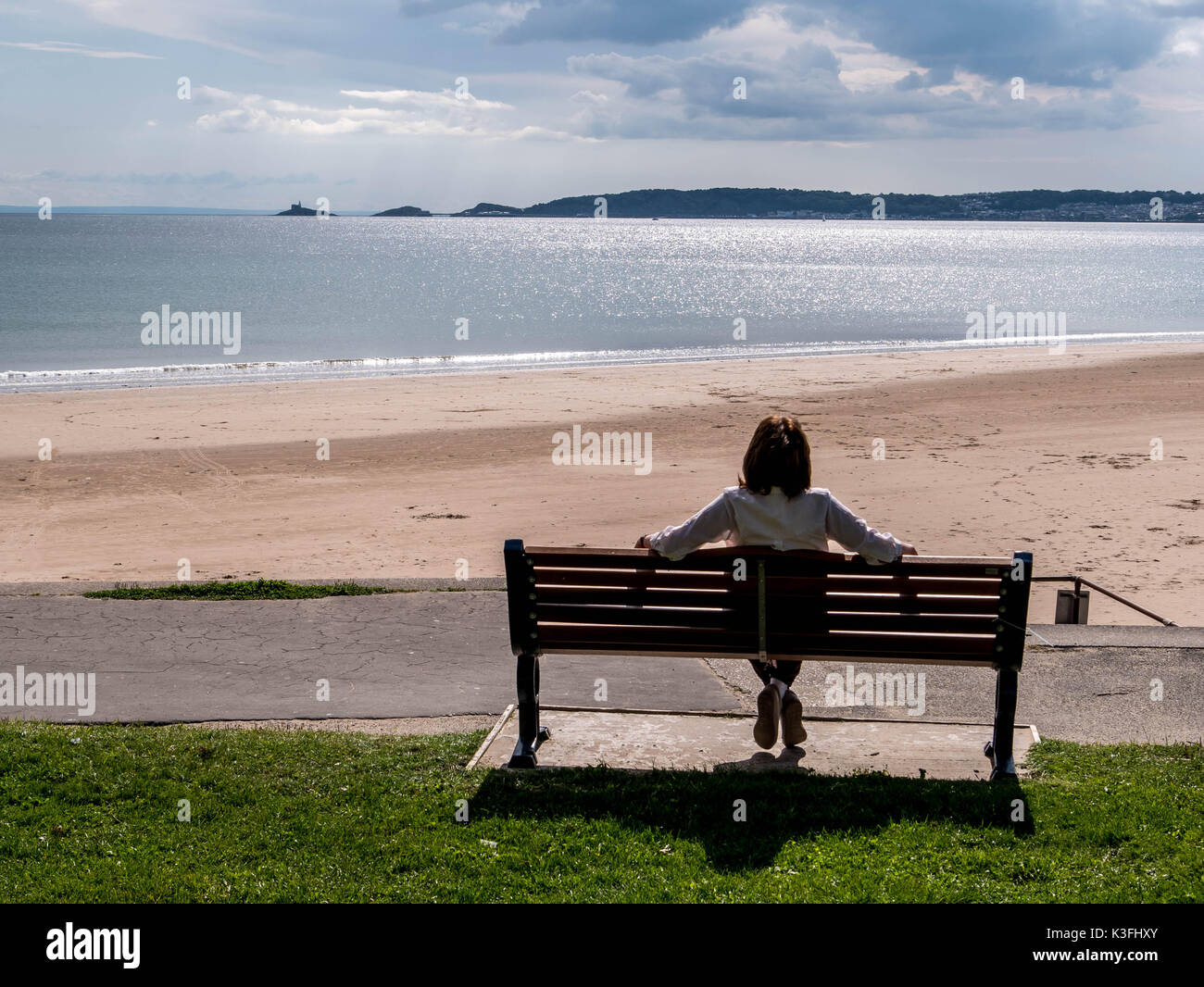 Coppia signora seduta sul sedile in legno che guarda verso Mumbles faro attraverso Swansea Bay con il Devon Coast a distanza Foto Stock