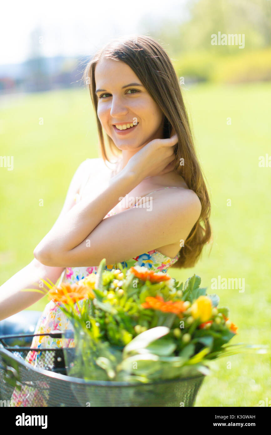 Ritratto di giovane bella donna con capelli lunghi in estate park. A fianco di una bicicletta con un cestino di fiori Foto Stock