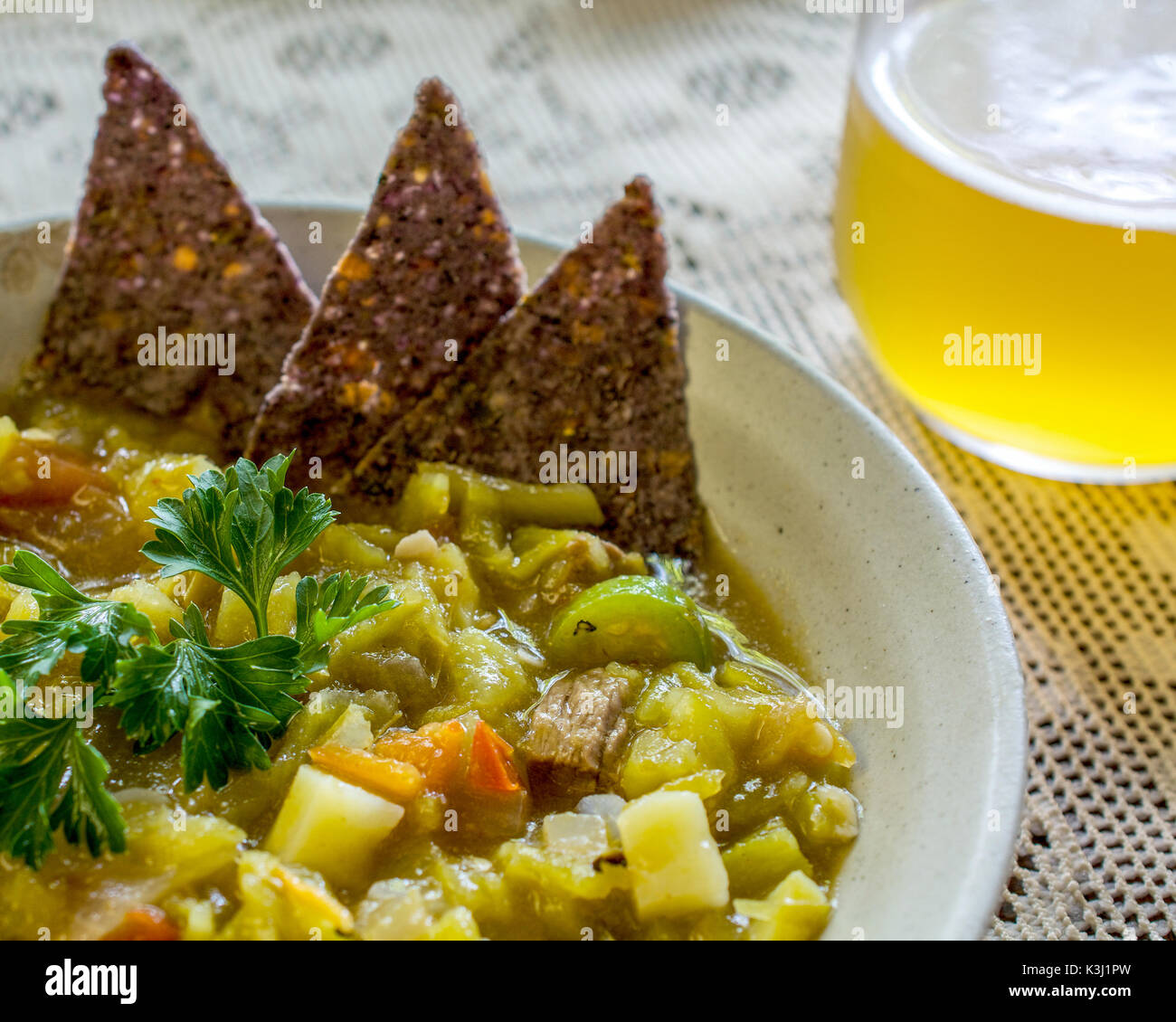 Primo piano sul messicano peperoncino stufato di tan ciotola decorata con blue tortilla di mais sulla tovaglia bianca servita con cucchiaio e birra - cucina etnica conce Foto Stock