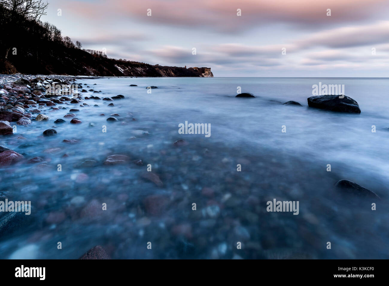 Tempo di esposizione lungo nella luce della sera del invernale costa ripida in cape Arkona su Rügen. In primo piano l'acqua del Mar Baltico e alcuni dei più grandi pietre, con sullo sfondo la ripida costa con il piccolo faro e nuvole speciale. Foto Stock