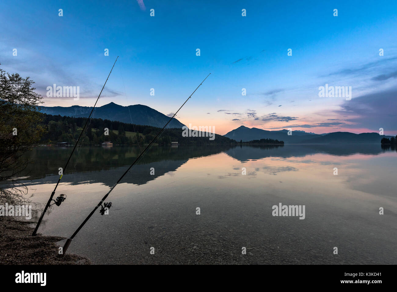 Due canne da pesca nel crepuscolo in cristalline Walchensee, nella penisola di sfondo Zwergern, Herzogstand e Jochberg. Foto Stock