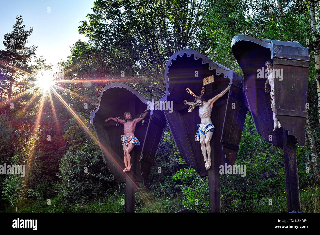 Il sole si rompe con forte irraggiamento solare attraverso gli alberi del backgrounIn fForeground una crocifissione di Gesù, carving, strada calvario Foto Stock