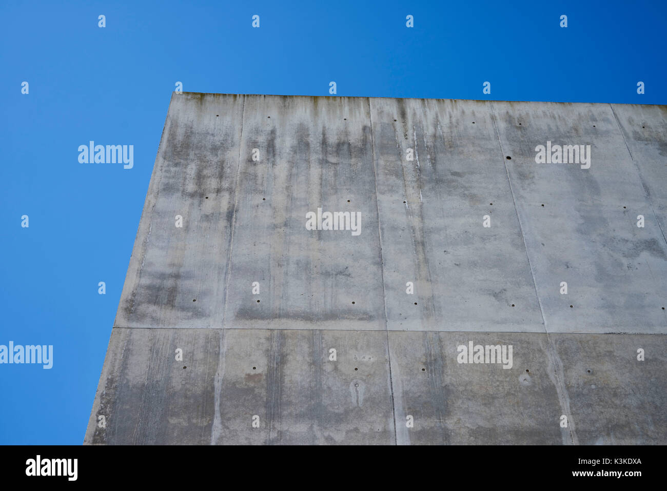 Calcestruzzo parete grigia con struttura e inclusioni come uno sfondo di fronte blu cielo privo di nuvole Foto Stock