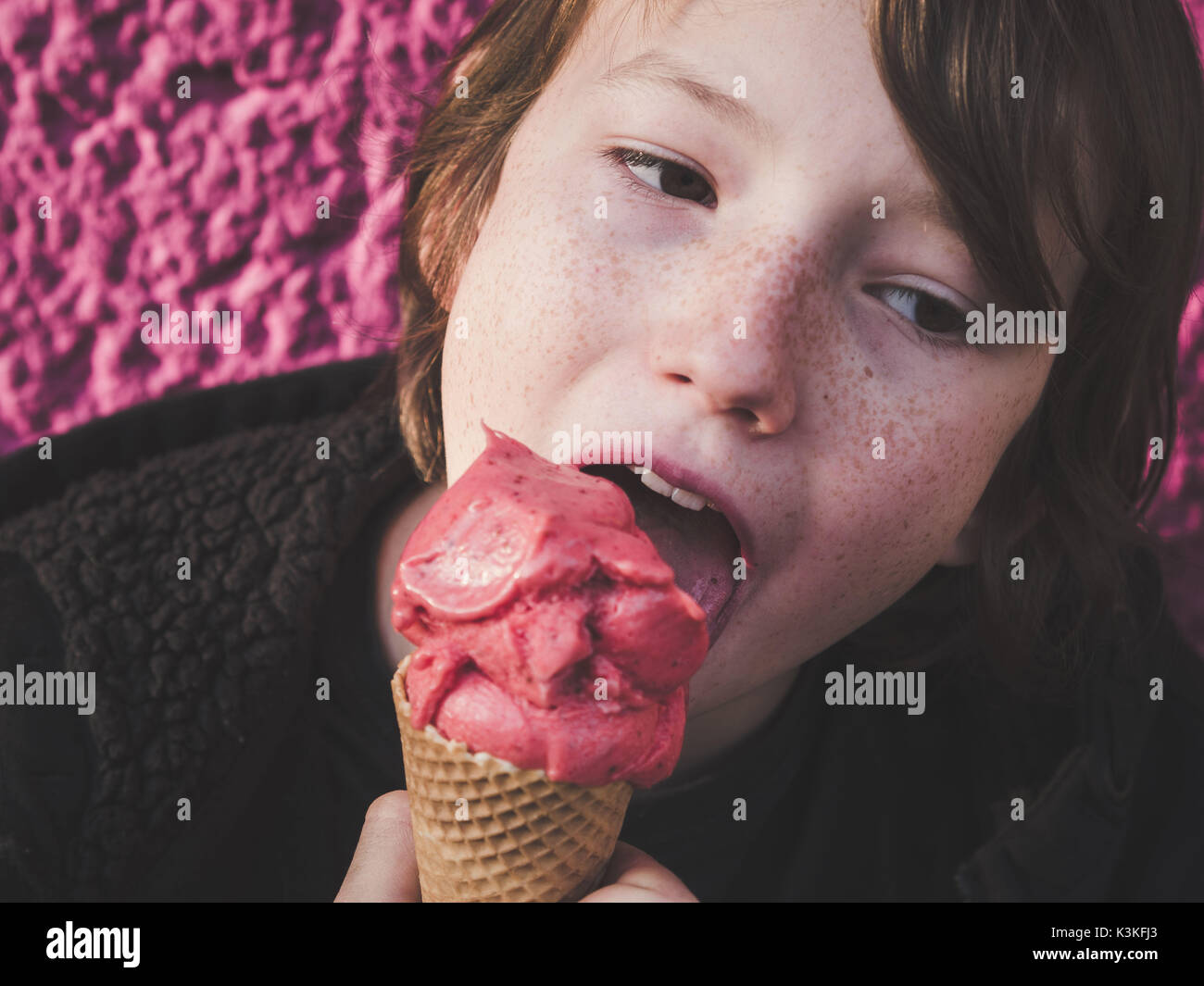 Ritratto di un giovane mangiare fragole gelato di fronte a sfondo rosa Foto Stock