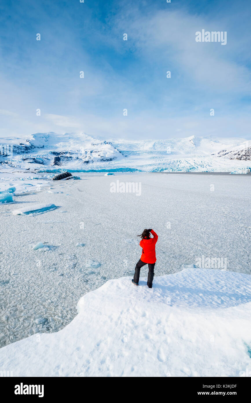 Fjallsarlon laguna glaciale, Est Islanda Islanda. Uomo con rivestimento rosso ammirando la vista della laguna gelata in inverno (MR). Foto Stock