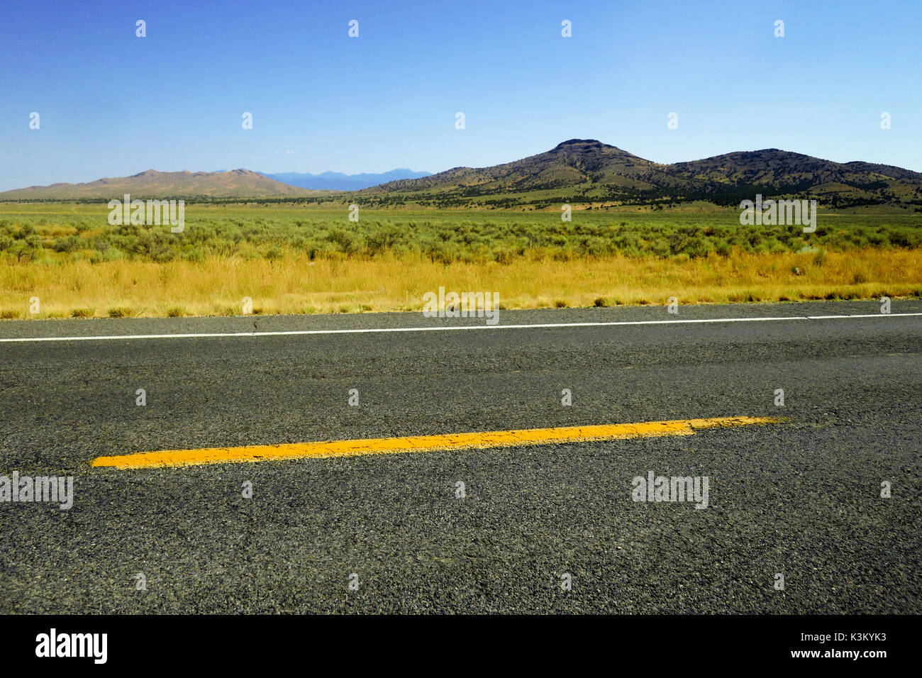 Una strada di fronte ad una pianura di erba scrub e una montagna dietro di esso nello Utah. Foto Stock