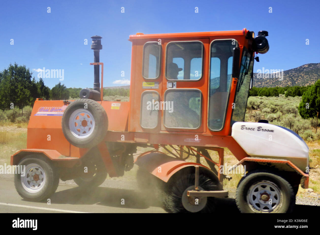 Un orange street sweeper la pulizia di una strada nel deserto per il resurfacing. Foto Stock