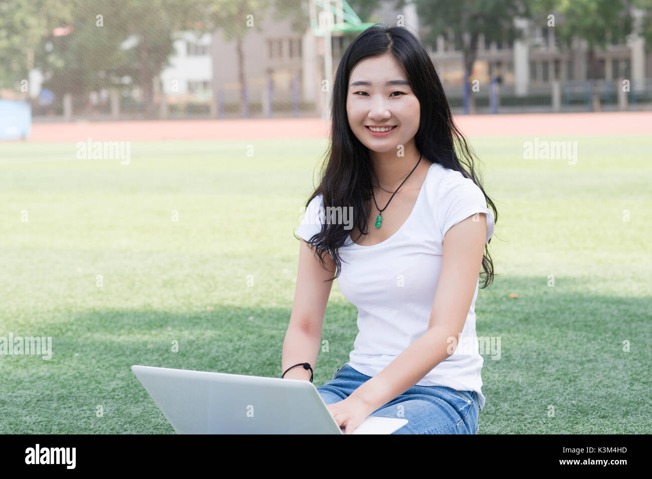 Bella asiatica studente di college con il computer portatile ,sat sul parco giochi. Foto Stock