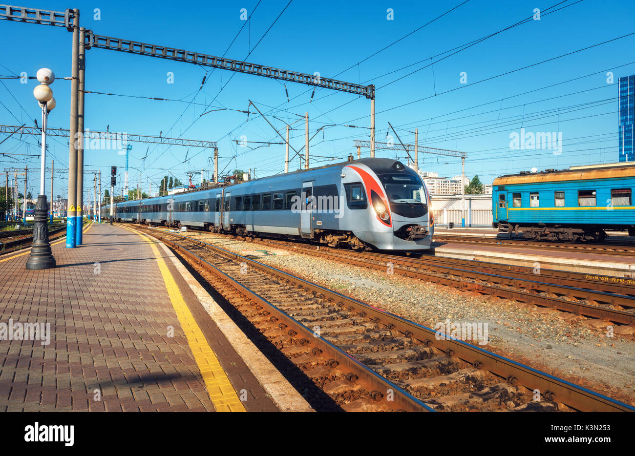 Treno ad alta velocità presso la stazione ferroviaria al tramonto in Europa. Moderno treno intercity sulla linea ferroviaria piattaforma. Scena urbana con bellissimo trai passeggero Foto Stock