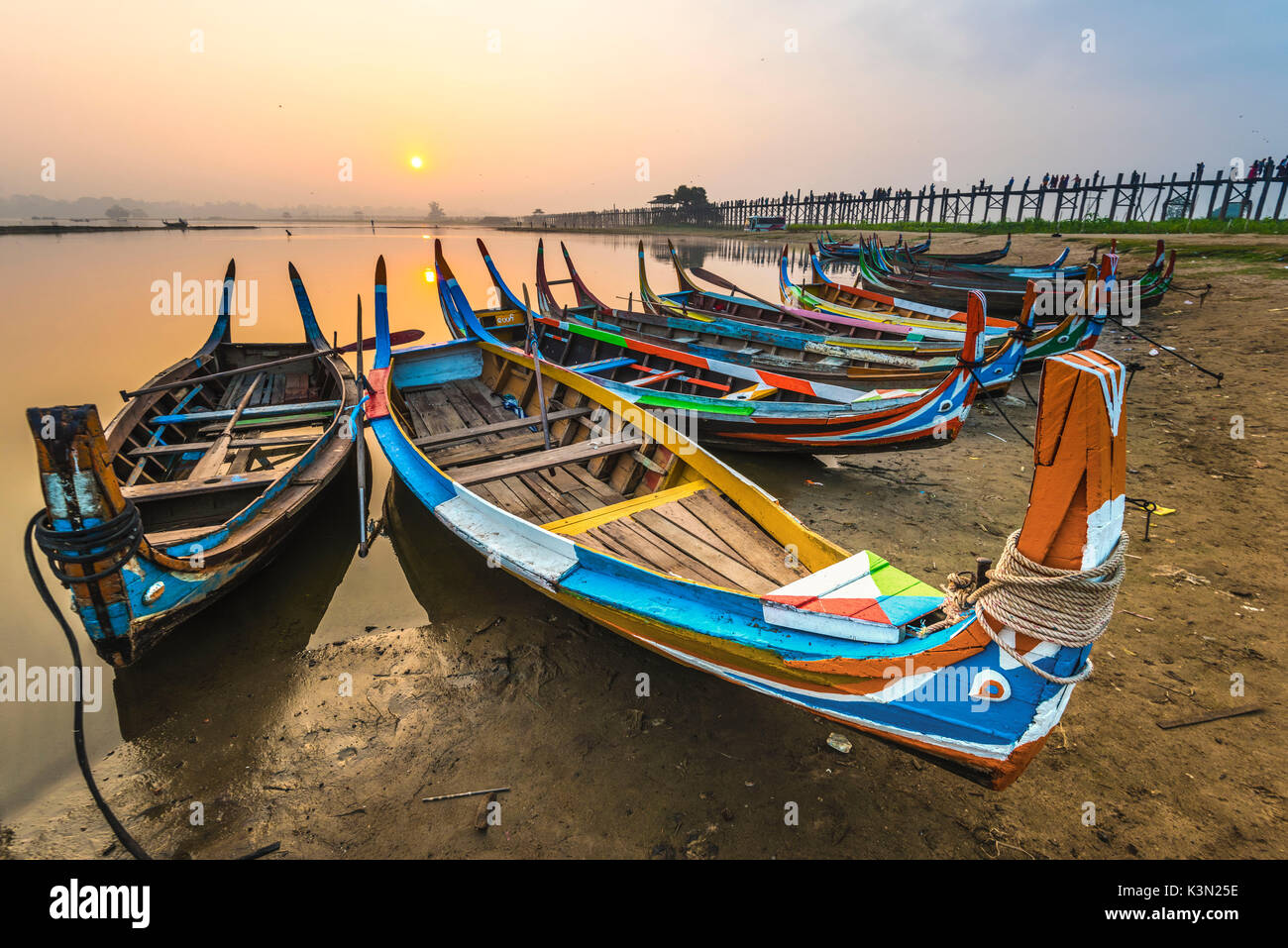 Amarapura, Mandalay regione, Myanmar. Barche colorate ormeggiato sulle rive del lago Taungthaman all'alba, con l'U Bein bridge in background. Foto Stock