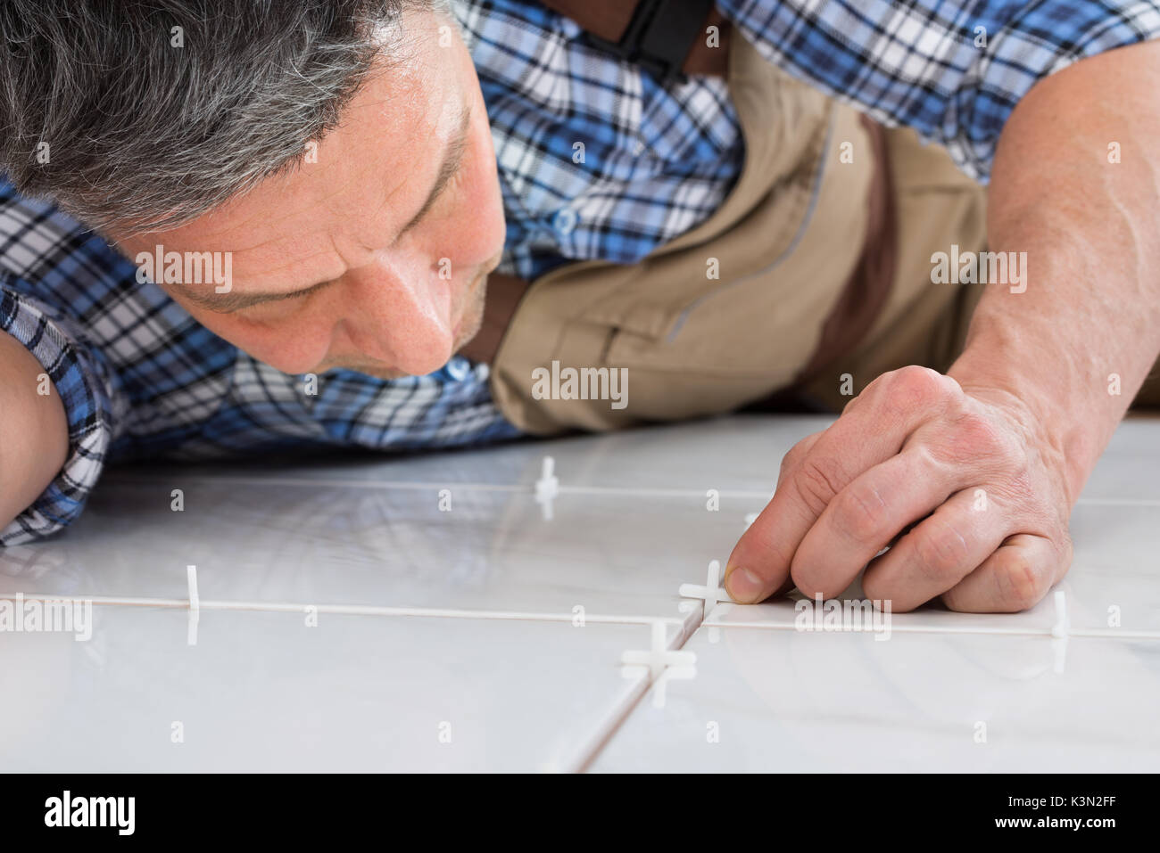 Close-up di un tuttofare giacente sul piano posizionando i distanziali tra le piastrelle Foto Stock