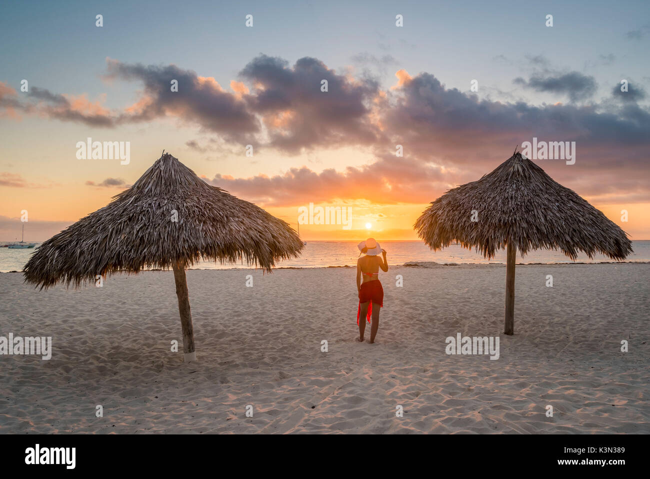 Bavaro Beach, Bavaro, Higuey, Punta Cana, Repubblica Dominicana. La donna da ombrelloni di paglia sulla spiaggia al tramonto (MR). Foto Stock