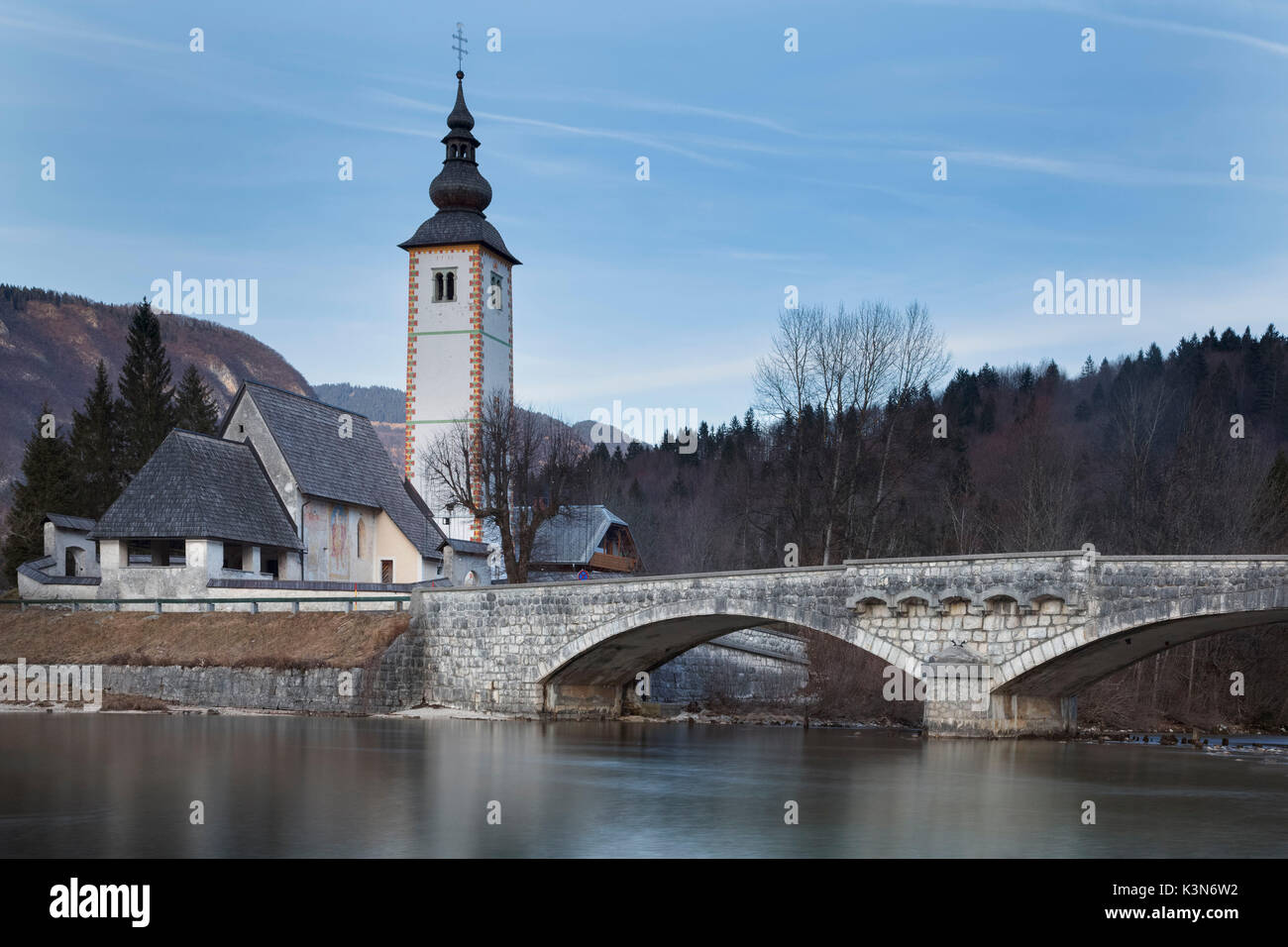 L'Europa, Slovenia Alta Carniola. Chiesa di Sv. Giovanni Battista e il ponte di pietra dal lago di Bohinj Foto Stock
