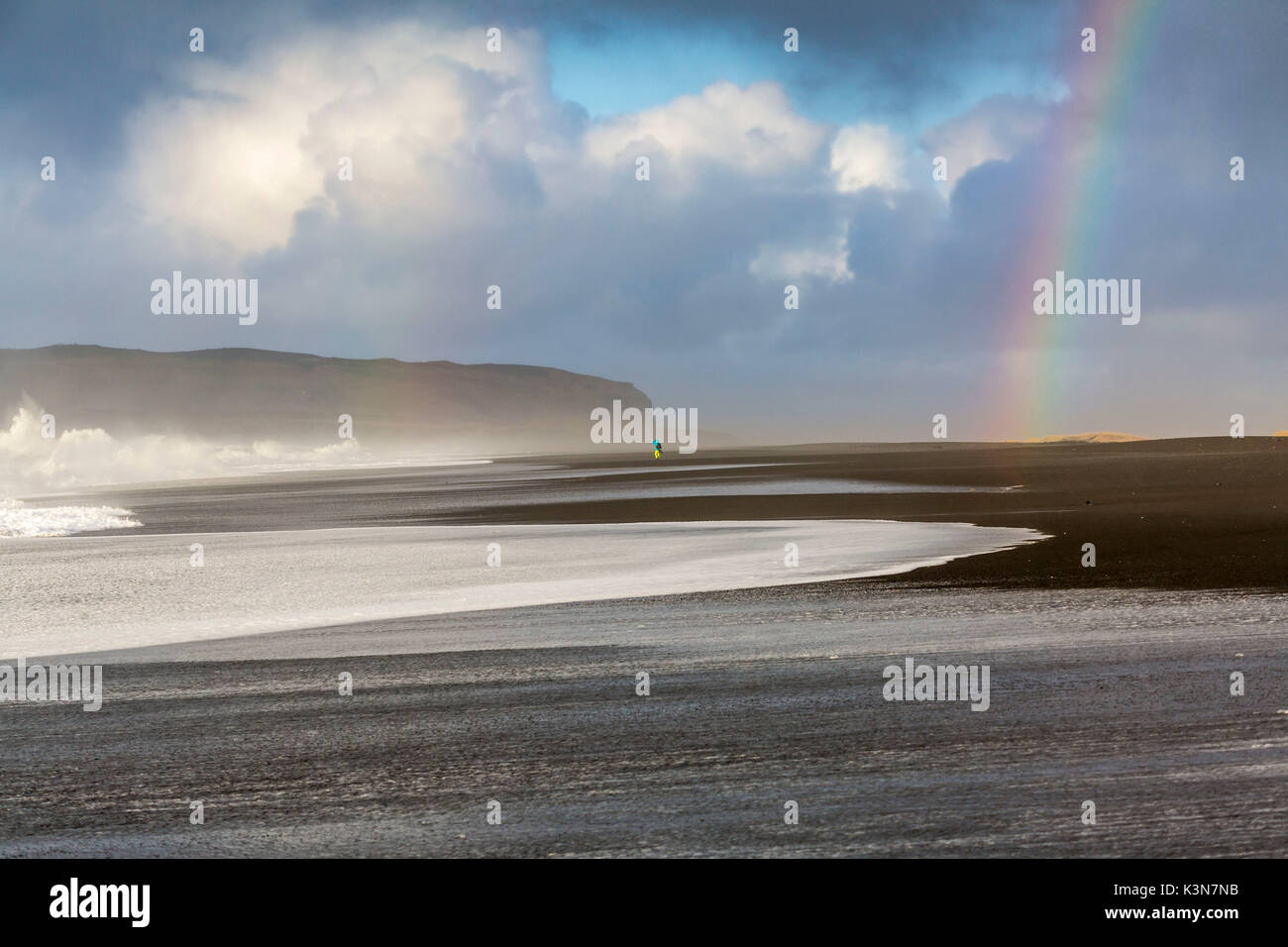 Un uomo è in cammino verso l'arcobaleno sulla spiaggia di Reynisfjara, Vik, Sudurland, Islanda, Europa Foto Stock