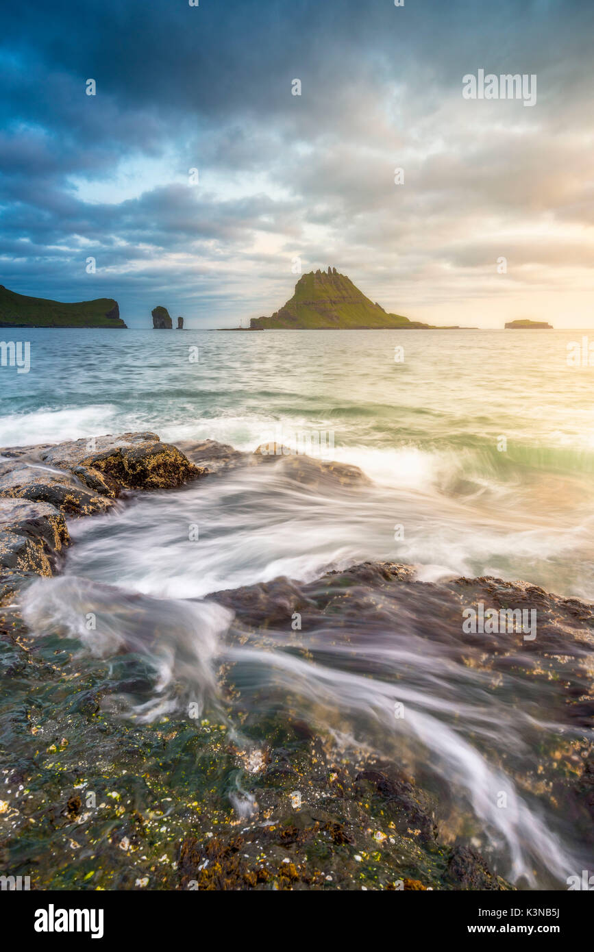 Funzionario Ministeriale isola, isole Faerøer, Danimarca. Rocce costiere con Tinholmur isolotto a sfondo al tramonto. Foto Stock