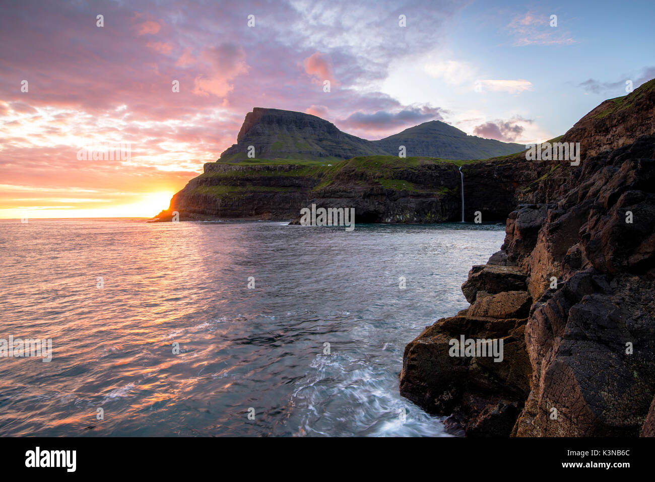 Gasadalur, funzionario ministeriale isola, isole Faerøer, Danimarca. La cascata iconica saltando dalla scogliera nell'oceano al tramonto. Foto Stock