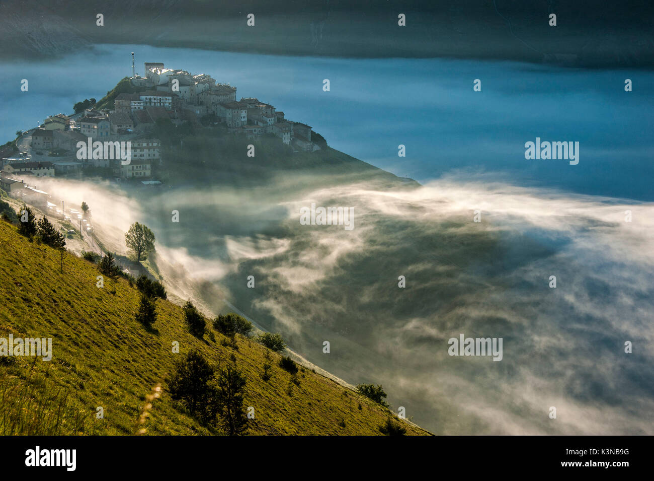 Il comune di Castelluccio di Norcia nella nebbia al tramonto, Monti Sibillni NP, Umbria, Italia Foto Stock