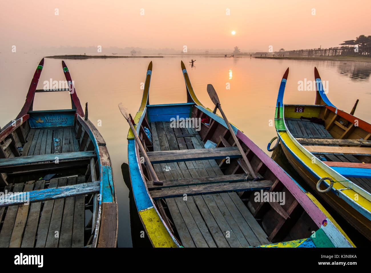 Amarapura, Mandalay regione, Myanmar. Barche colorate ormeggiato sulle rive del lago Taungthaman all'alba, con l'U Bein bridge in background. Foto Stock