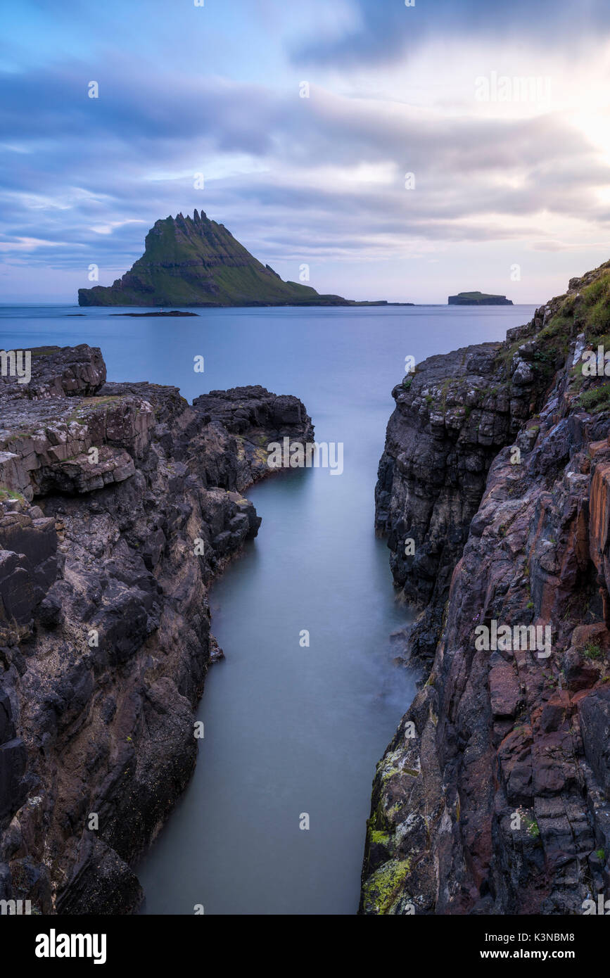 Funzionario Ministeriale isola, isole Faerøer, Danimarca. Rocce costiere con Tinholmur isolotto a sfondo al tramonto. Foto Stock