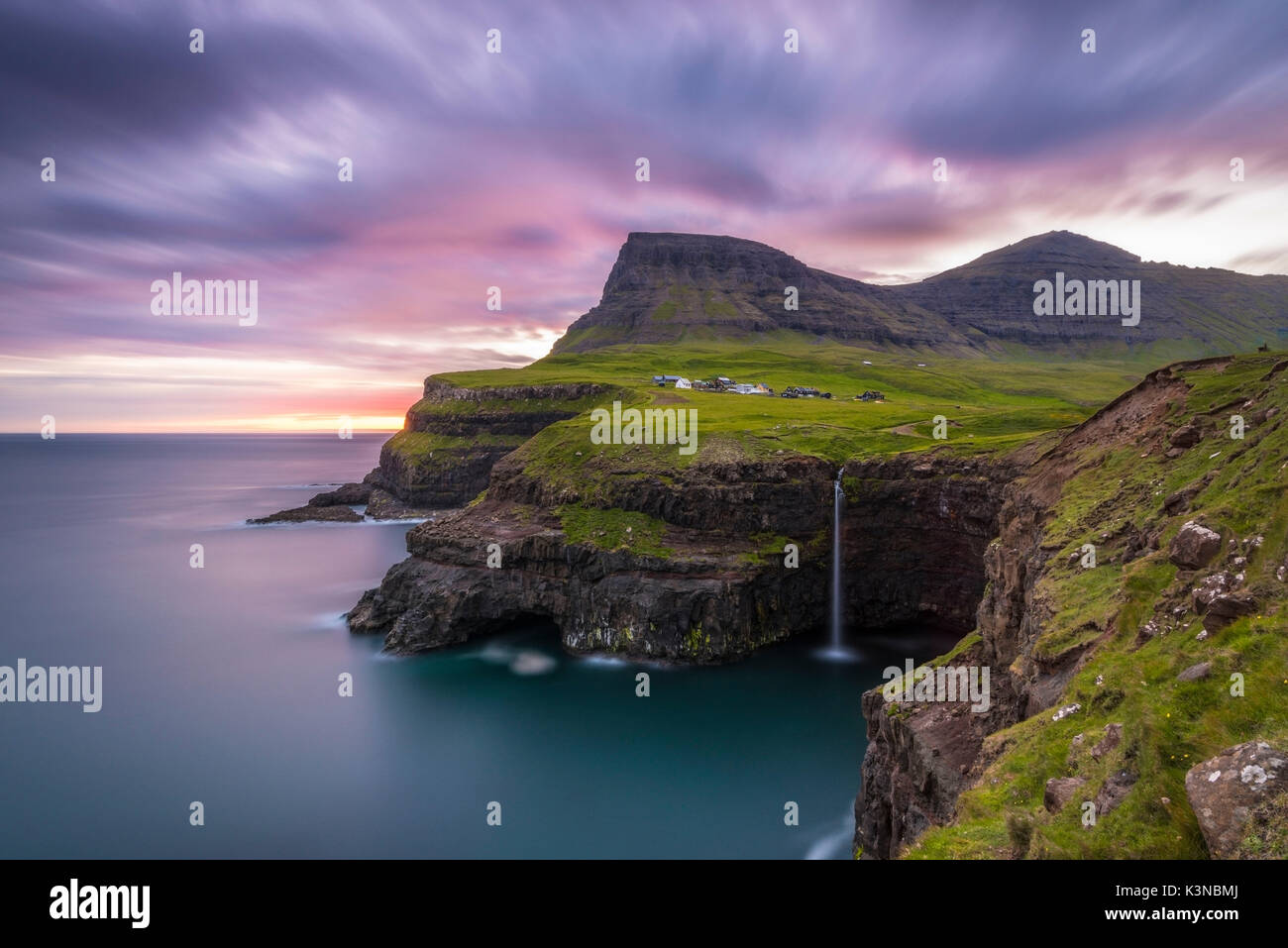 Gasadalur, funzionario ministeriale isola, isole Faerøer, Danimarca. La cascata iconica saltando dalla scogliera nell'oceano al tramonto. Foto Stock