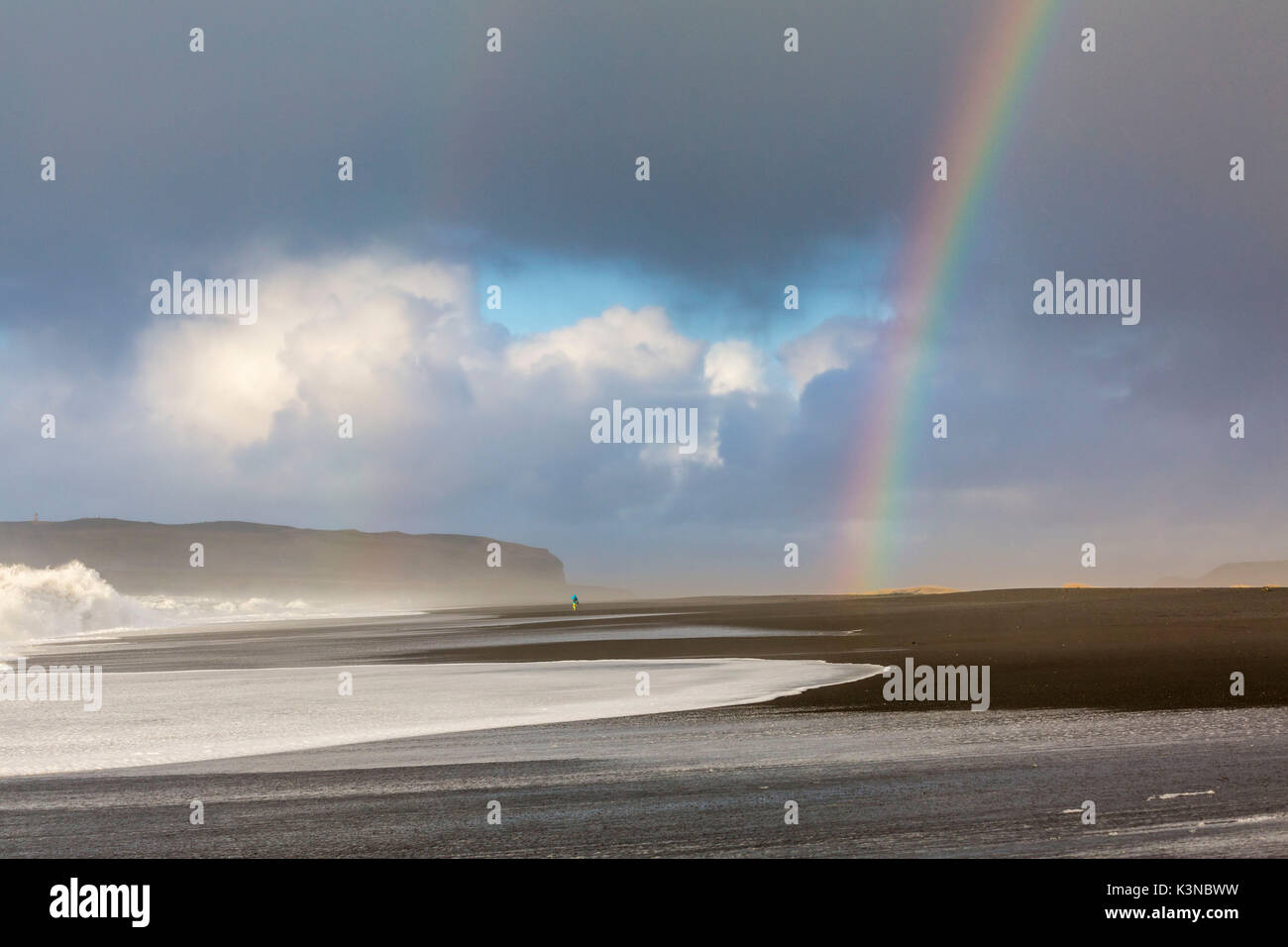 Un uomo è in cammino verso l'arcobaleno sulla spiaggia di Reynisfjara, Vik, Sudurland, Islanda, Europa Foto Stock