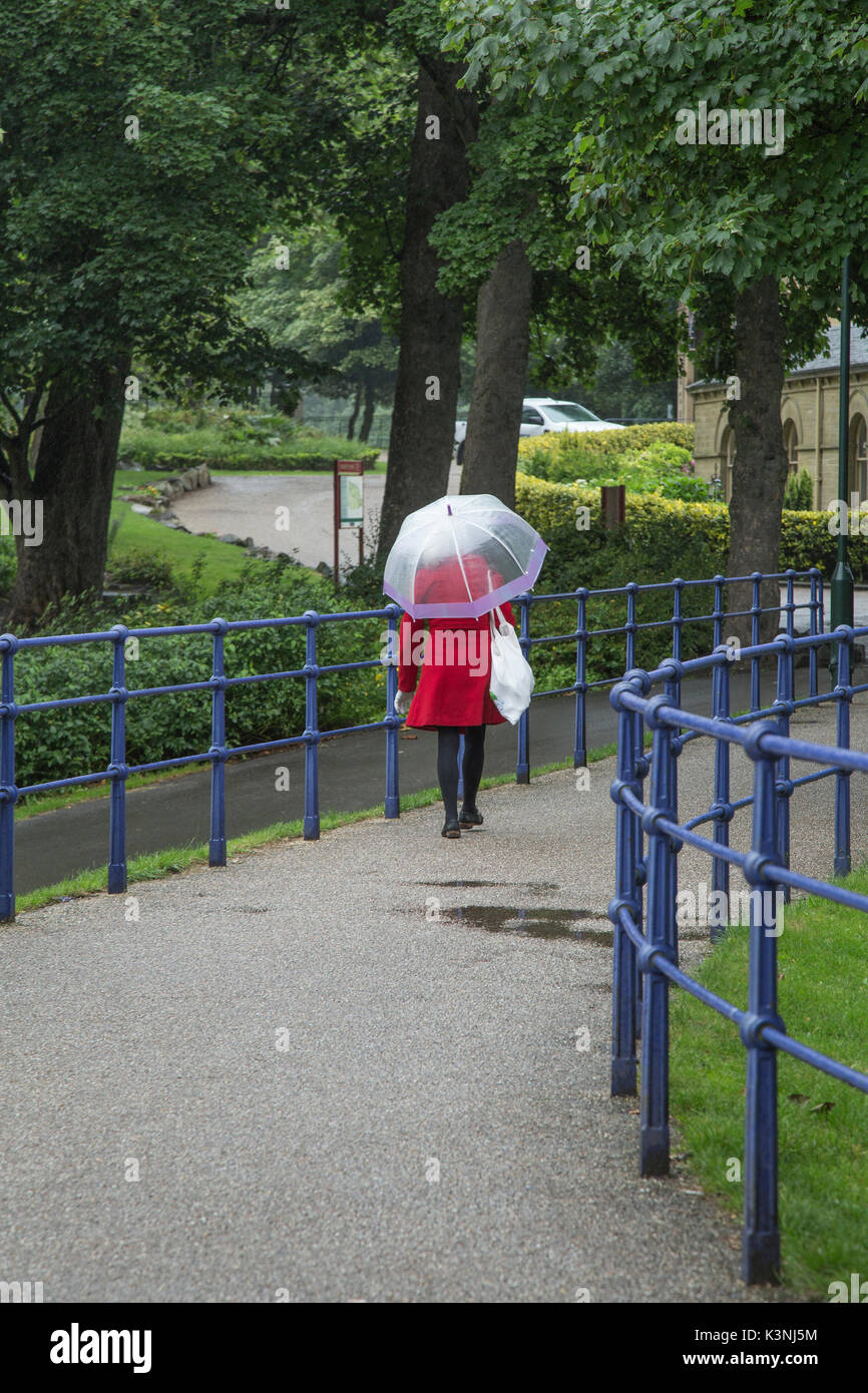 Una signora è a piedi sotto la pioggia lungo un percorso che porta un ombrello Foto Stock