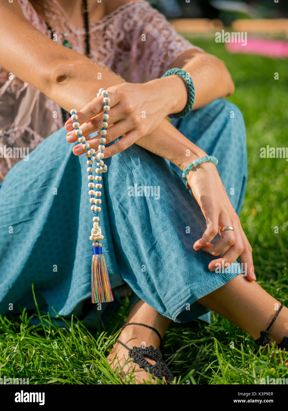 Donna, lit lato vicino, conta Malas, filamenti di perline di legno impiegati per mantenere il conteggio durante il mantra meditazioni. Il buddismo. Ragazza seduta nel parco un Foto Stock