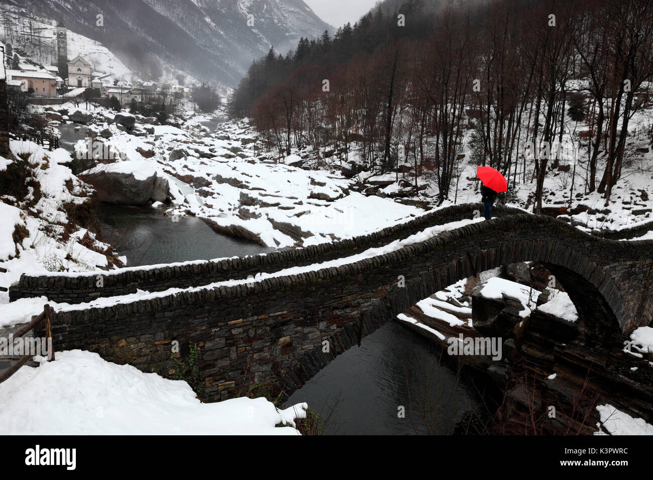 Ragazza con un ombrello rosso sul Ponte dei salti di Lavertezzo in inverno in Val Verzasca, Ticino, Svizzera Foto Stock