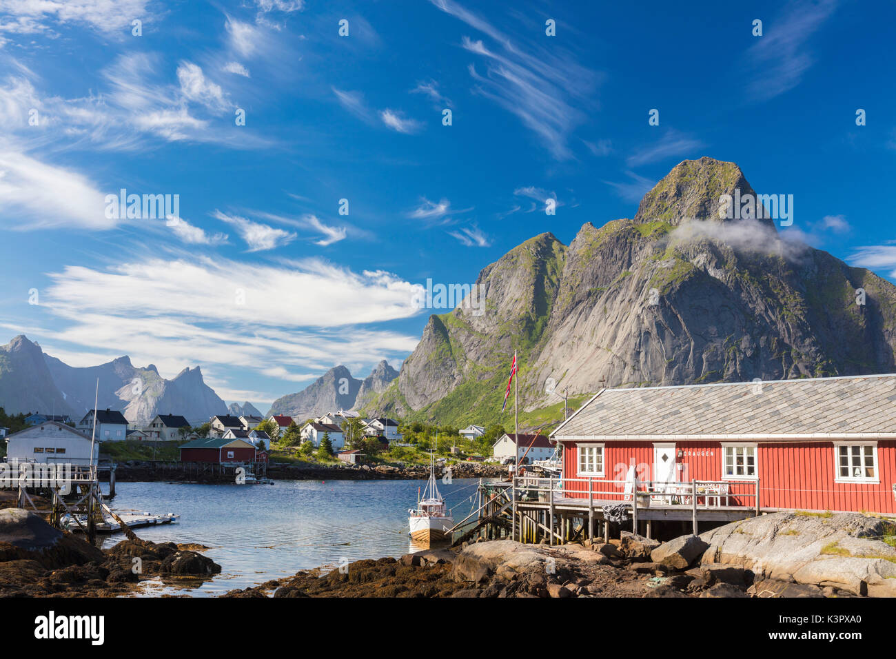 Casa tipica di pescatori chiamato Rorbu incorniciato da picchi rocciosi e mare blu Reine Moskenes Isole Lofoten in Norvegia Europa Foto Stock
