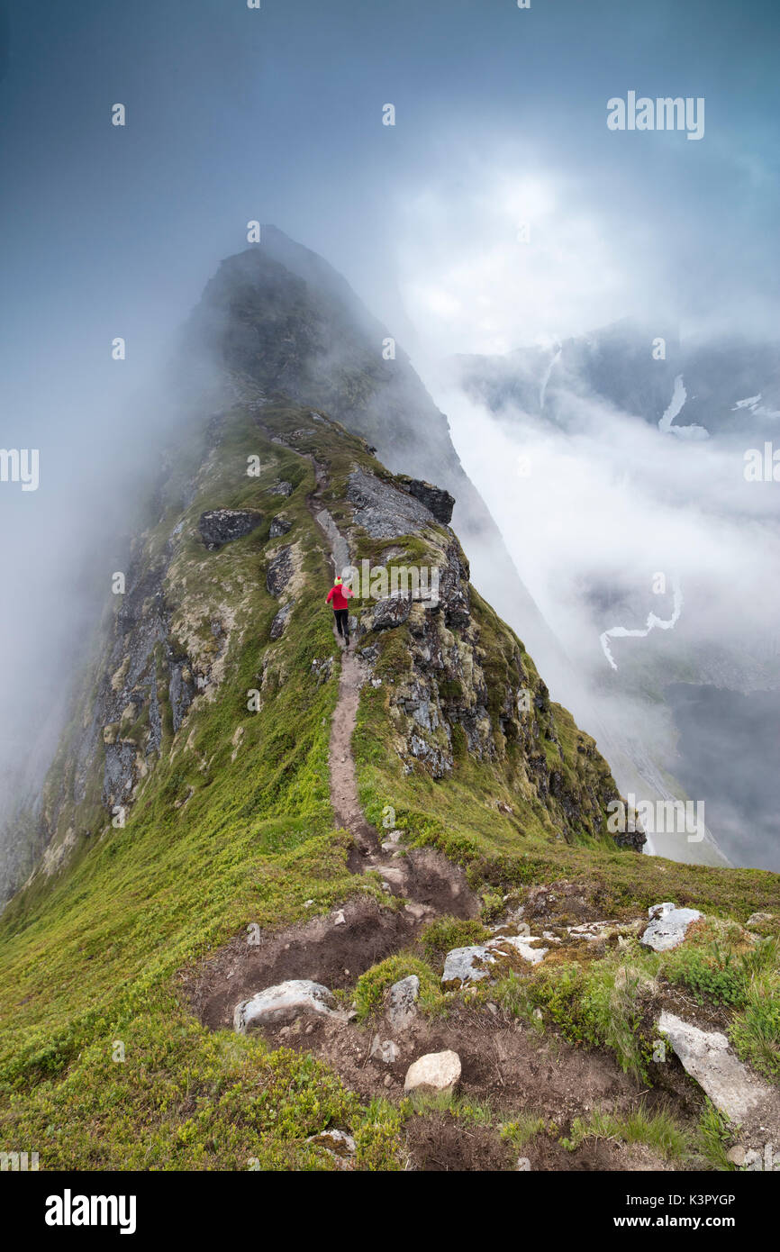 Escursionista gira su un ripido sentiero per raggiungere la vetta del monte Reinebringen sotto la nebbia Moskenes Isole Lofoten in Norvegia Europa Foto Stock