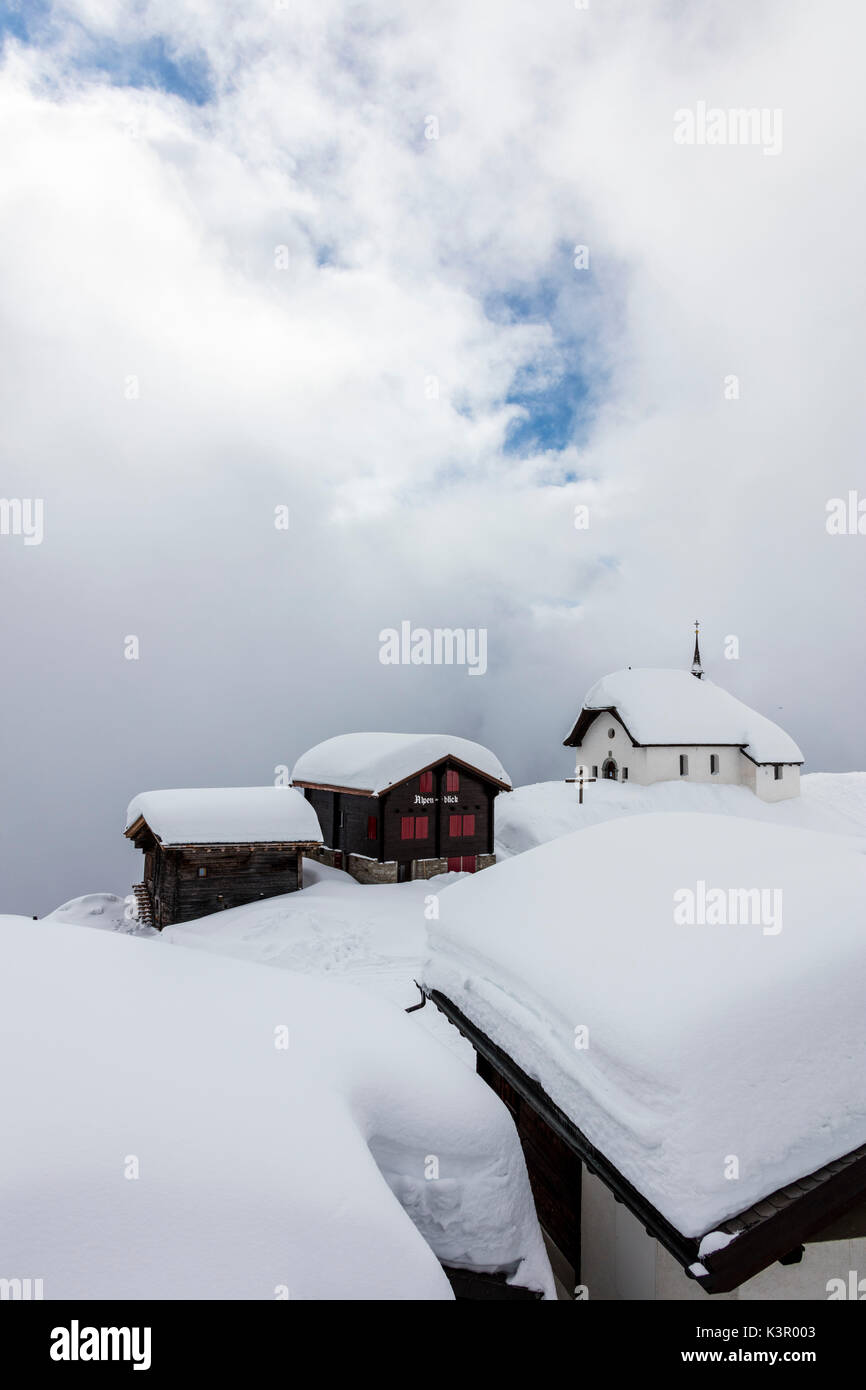 Coperta di neve rifugi di montagna e chiesa circondato da nuvole basse Bettmeralp distretto di Raron nel canton Vallese Svizzera Europa Foto Stock