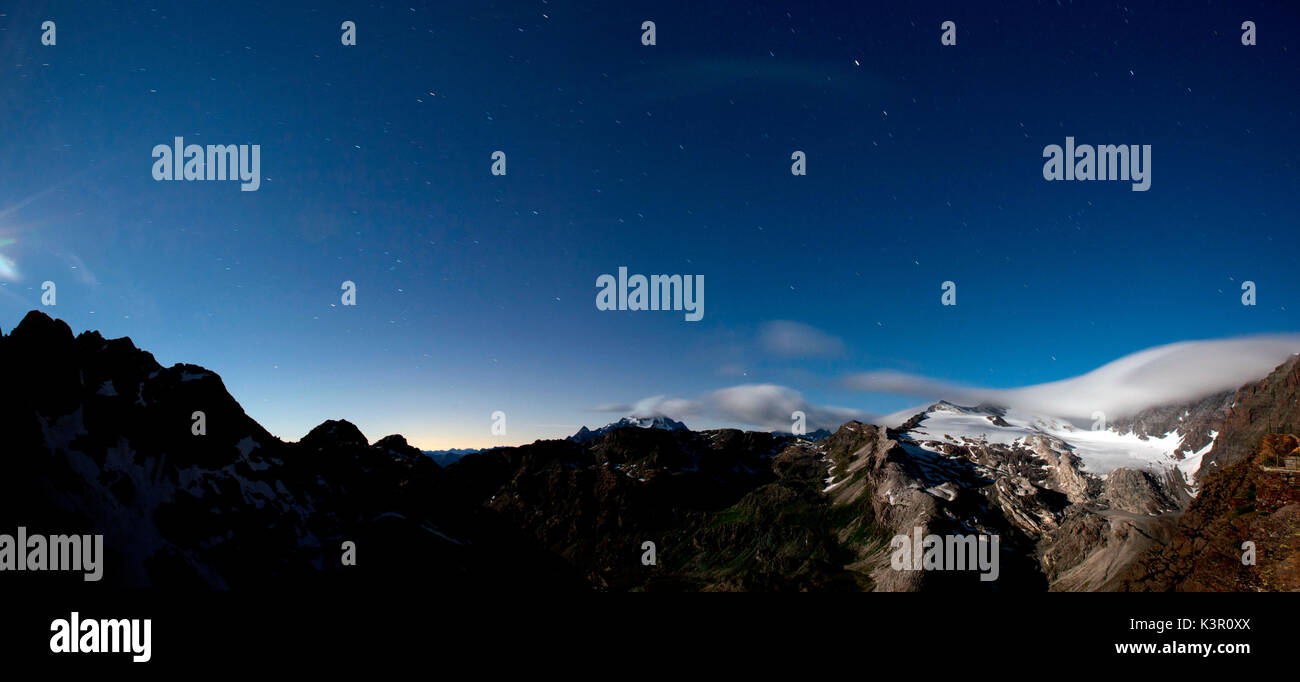 Guardando il cielo pieno di stelle in una chiara notte dal rifugio Martinelli, le nuvole sono in movimento sul ghiacciaio di Scerscen e della distanza è possibile vedere anche il Monte Disgrazia, VALMALENCO Lombardia, Italia. Europa Foto Stock