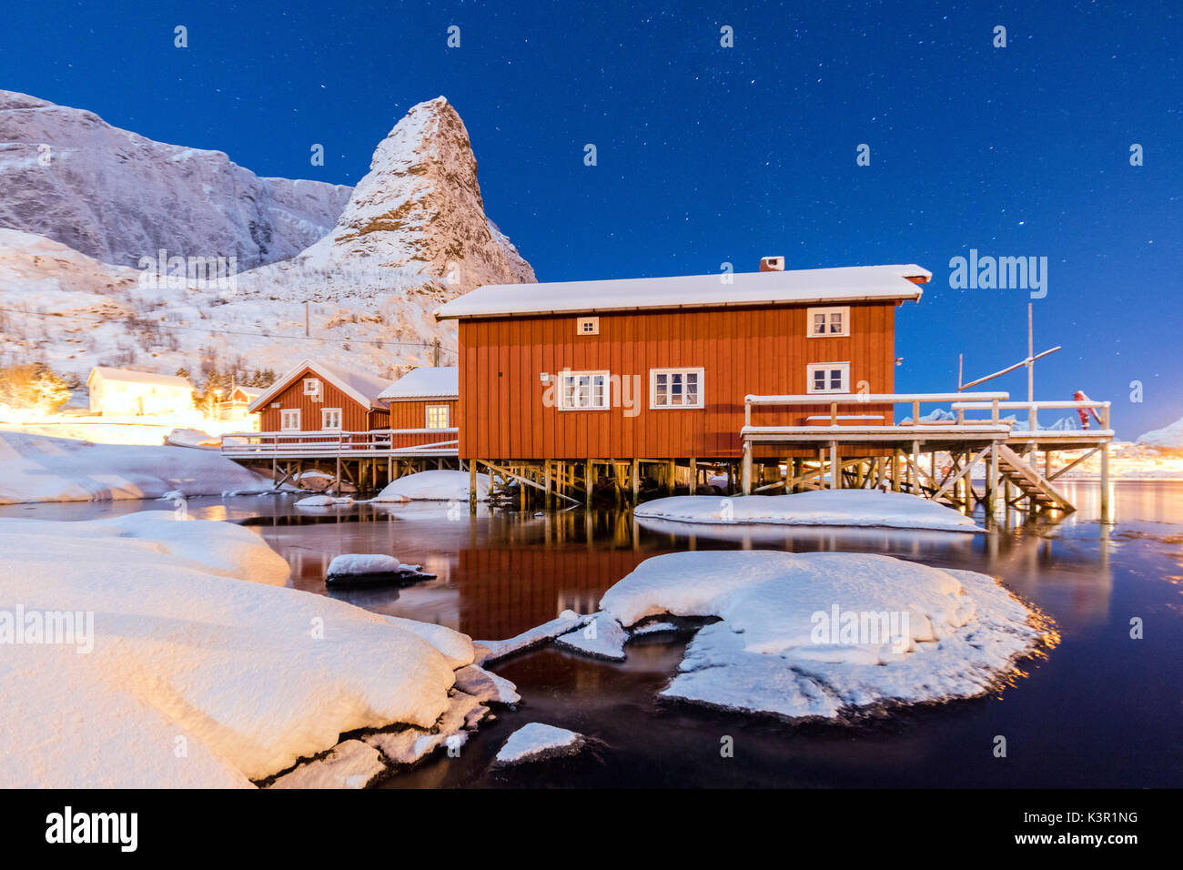 Notte stellata sulle cime innevate circondata dal mare ghiacciato e case di pescatori Reinevagen Baia delle Isole Lofoten in Norvegia Europa Foto Stock