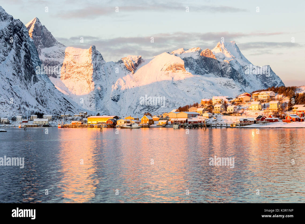 Il colore rosa di sunrise e cime innevate si riflettono nel mare freddo Reine Bay Nordland Isole Lofoten in Norvegia Europa Foto Stock