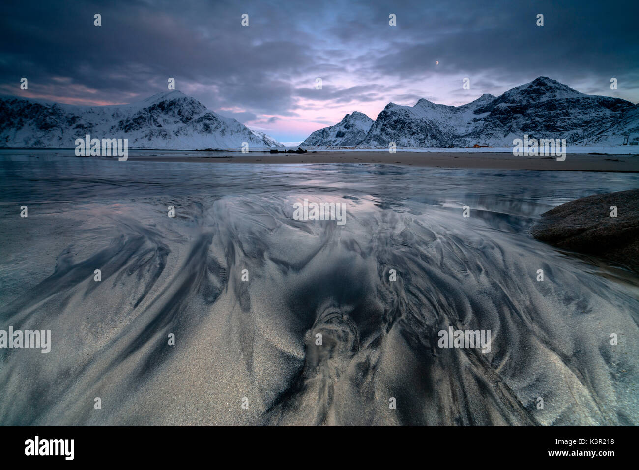 Le onde e il ghiaccio nel surreale Skagsanden spiaggia circondata da vette innevate Flakstad Nordland county Isole Lofoten in Norvegia Europa Foto Stock