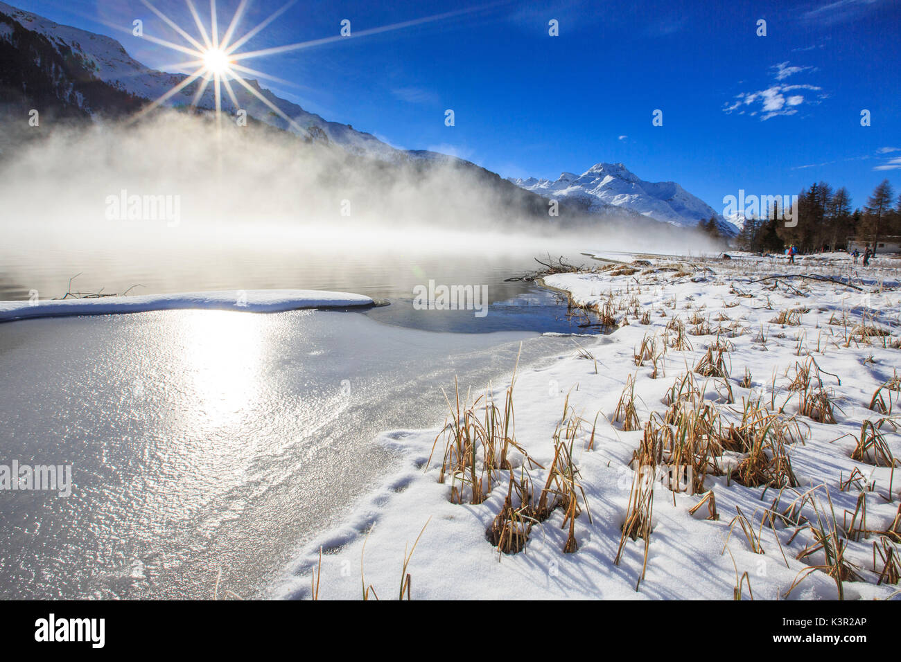 Inverno il sole illumina il lago ghiacciato di Silvaplana circondato da nebbia Maloja Cantone dei Grigioni Engadina Svizzera Europa Foto Stock