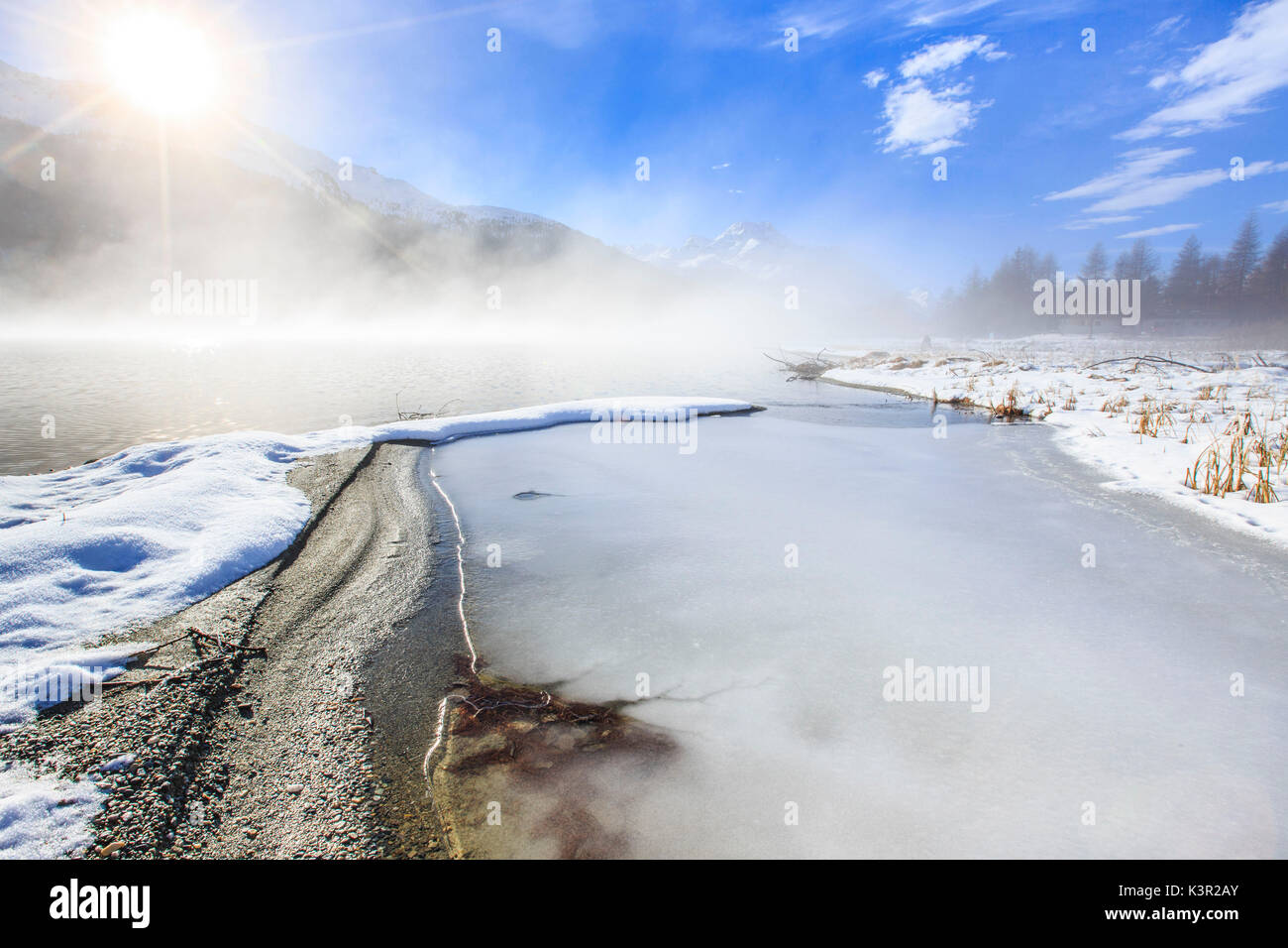 Inverno il sole illumina il lago ghiacciato di Silvaplana circondato da nebbia Maloja Cantone dei Grigioni Engadina Svizzera Europa Foto Stock