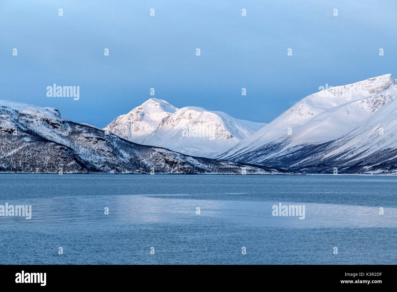 Cielo blu e vette innevate circondano il mare freddo Alpi Lyngen Tromsø Lapponia Norvegia Europa Foto Stock