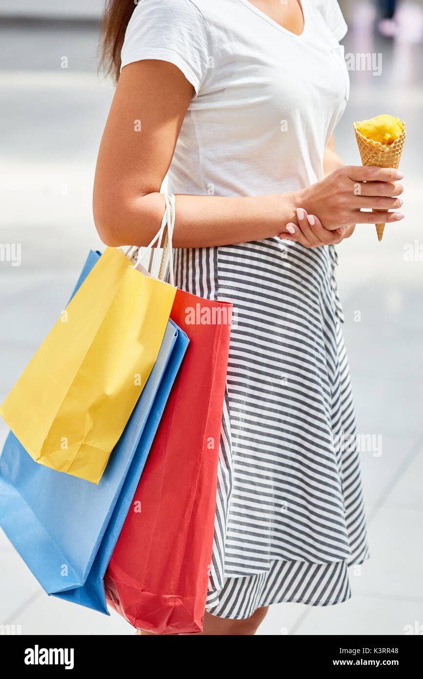 La sezione centrale verticale del prety giovane donna in piedi nel centro commerciale azienda di sacchetti di carta e cono gelato Foto Stock