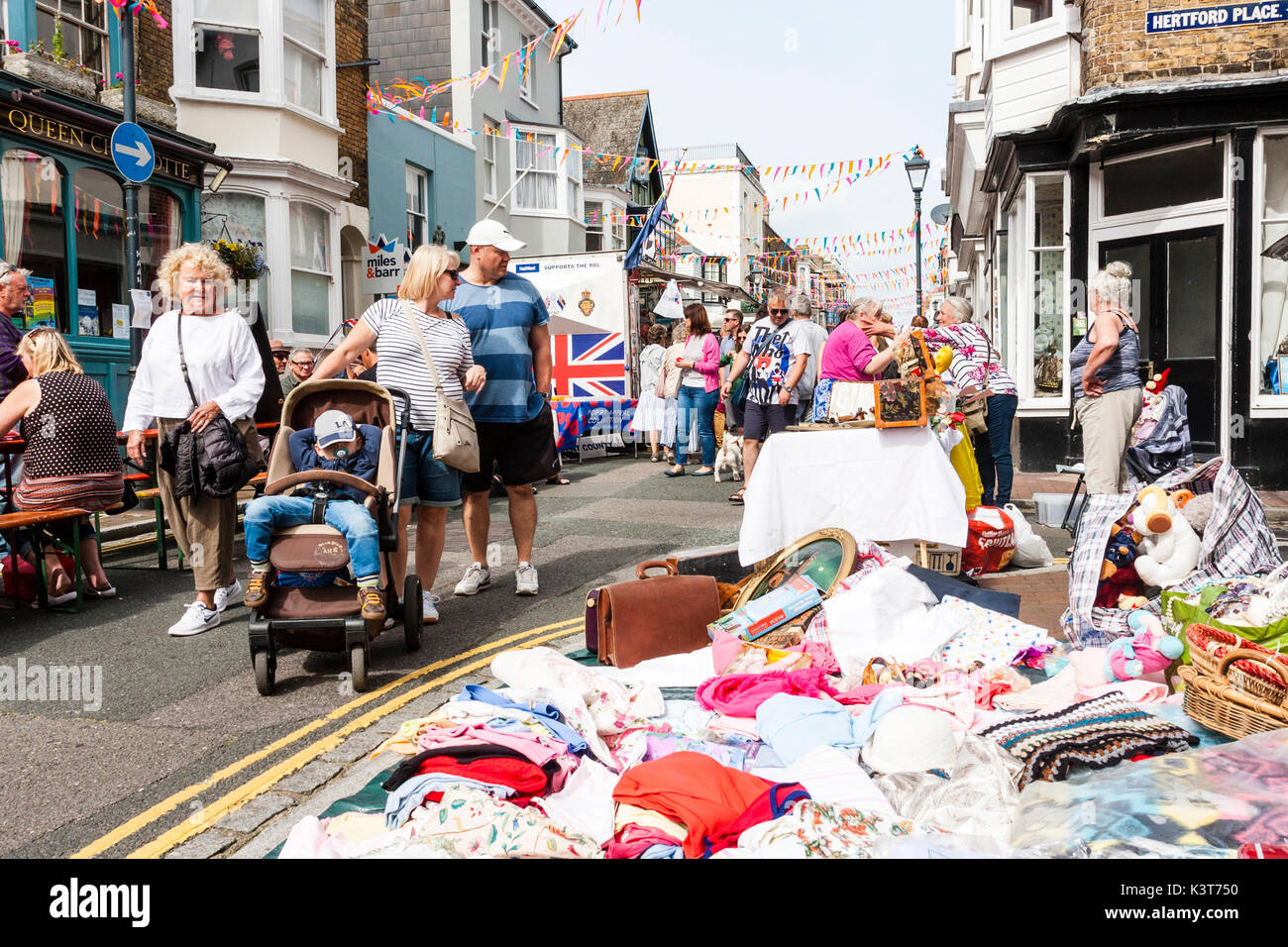 Cittadina inglese street fair. Strada stretta con bancarelle con gli operatori economici e la gente del luogo di vendita. La strada affollata, diurno e il sole. Bunting appeso tra gli edifici. Foto Stock